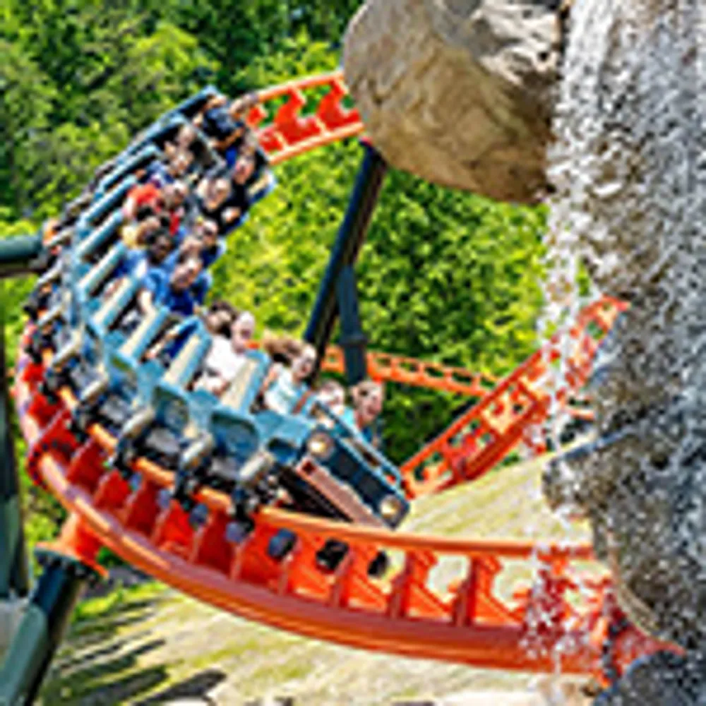 Riders are experiencing an exciting loop on a roller coaster near a rock and waterfall feature