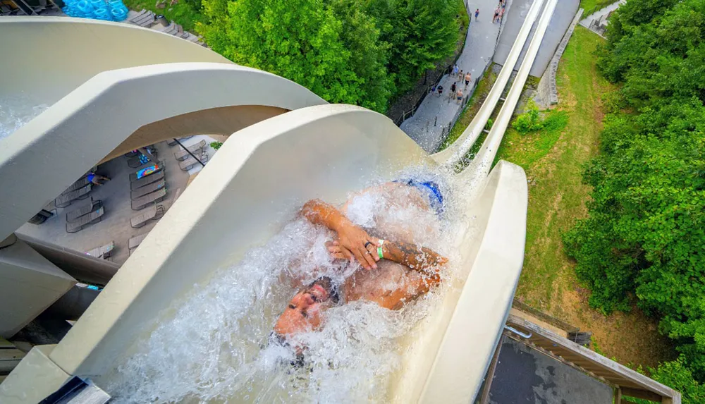 In this image a person is enjoying a thrilling ride down a winding water slide at an amusement park with a birds-eye view emphasizing the height and curvature of the slide