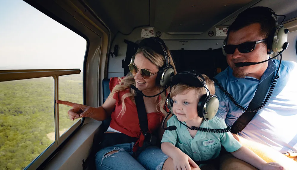 Two adults and a child are wearing headphones while enjoying a scenic helicopter flight