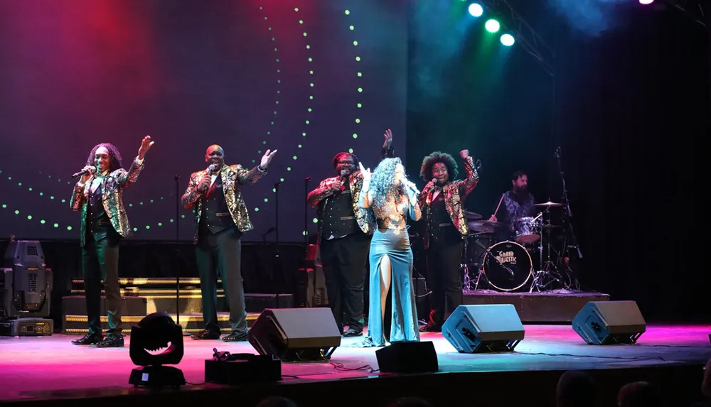 A group of performers is singing on stage with colorful lights in the background