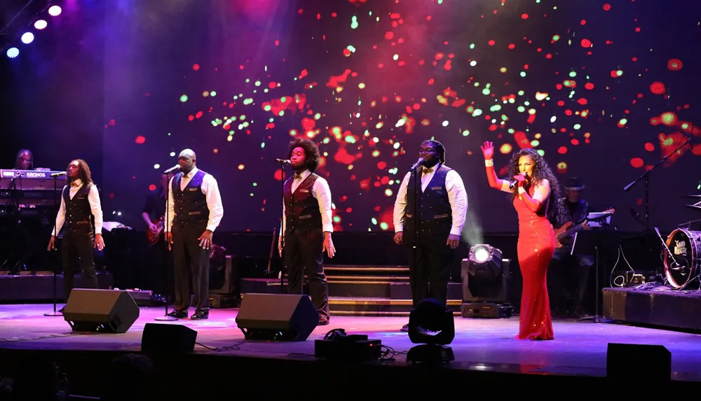 A group of performers are singing on stage under colorful stage lighting