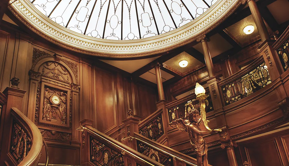 The image shows an ornately carved wooden staircase with a statue holding a lamp under an elegant circular skylight exuding a luxurious classical ambiance