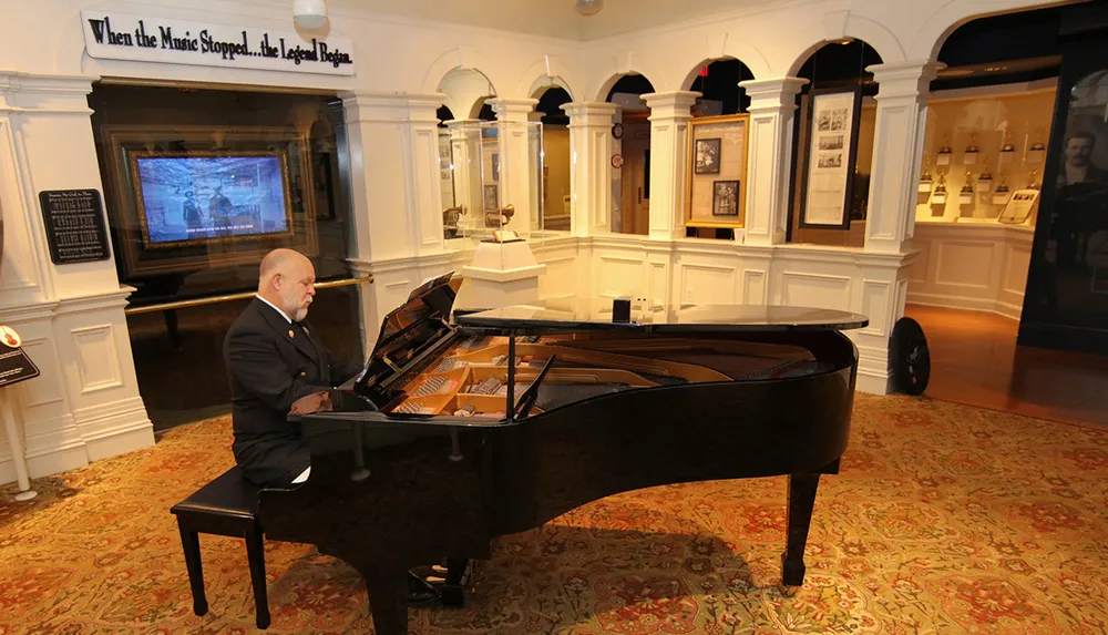 A man in formal attire is playing a grand piano in an elegant room that appears to be part of a museum or historical exhibit as suggested by display cases and information plaques