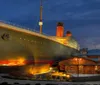 The image shows a replica of the Titanic at the Titanic Museum illuminated against a twilight sky