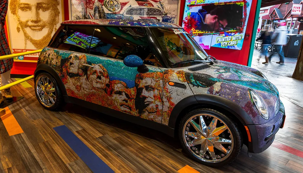 An intricately decorated Mini Cooper with a vibrant glittering mosaic design is on display in an indoor setting that includes various artworks