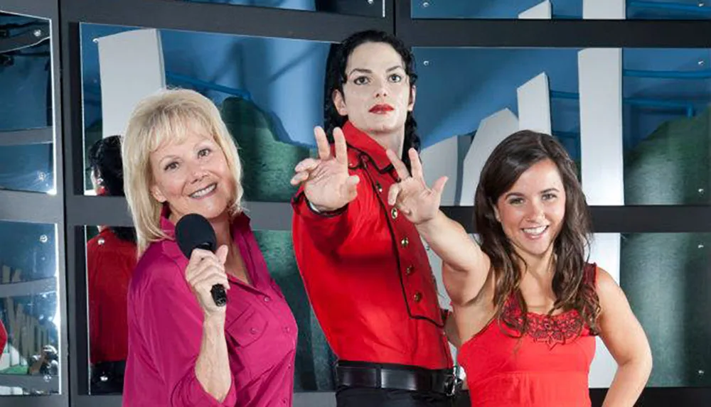 Two women are smiling and posing with a wax figure of a male pop star icon who is also dressed in his signature performance attire