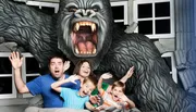 A family is posing with exaggerated expressions of fear as if they are being attacked by a large gorilla, in what looks to be a staged amusement park photo opportunity.