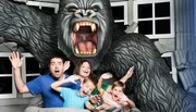 A family is posing with exaggerated expressions of fear as if they are being attacked by a large gorilla, in what looks to be a staged amusement park photo opportunity.