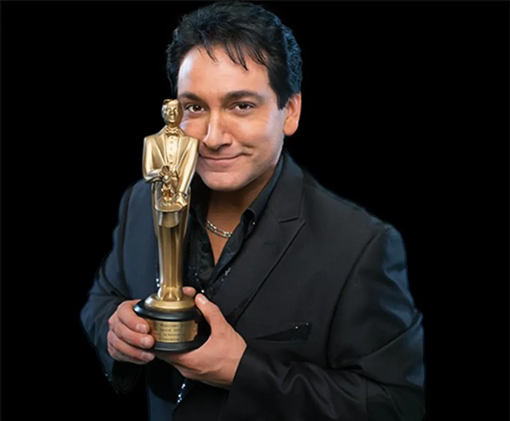 A person is smiling and holding a trophy that resembles an Oscar award