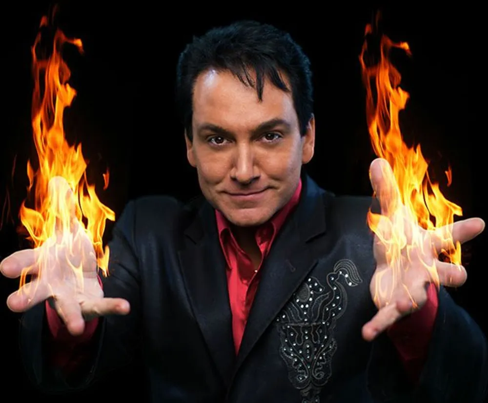 A person is presenting an illusion of holding flames in their hands with a confident smile against a black background