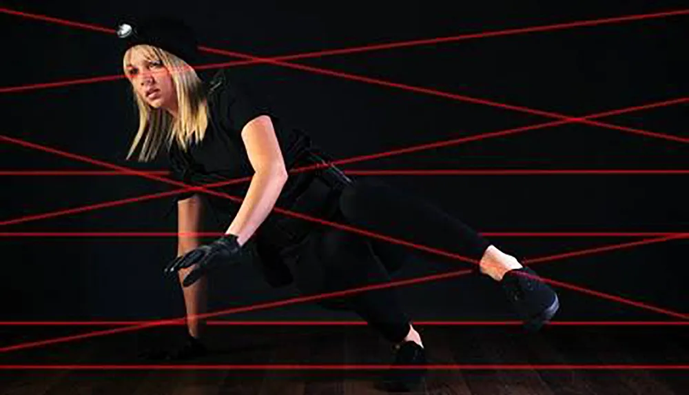 A person is crouched and maneuvering through a network of laser beams in a high-security or simulation setup