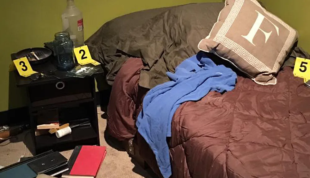 The image shows an unmade bed and a cluttered nightstand with items labeled with numbers suggesting a humorous imitation of a crime scene investigation in a domestic setting