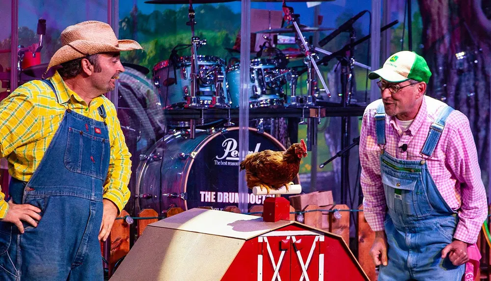 Two men in farmer attire are watching a chicken that appears to be playing a mini red piano on a stage with a drum set in the background