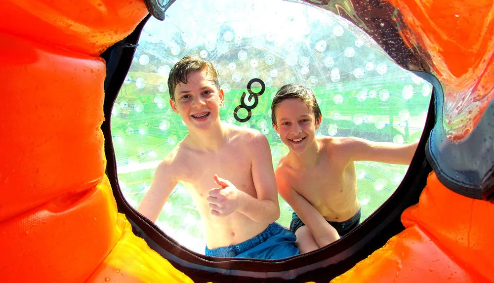 Two boys are smiling and giving a thumbs-up while inside a transparent inflatable water walking ball