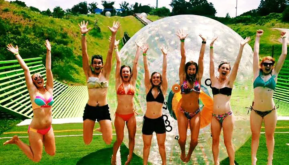 A group of people are joyfully jumping in the air in front of a large transparent inflatable ball on a sunny day