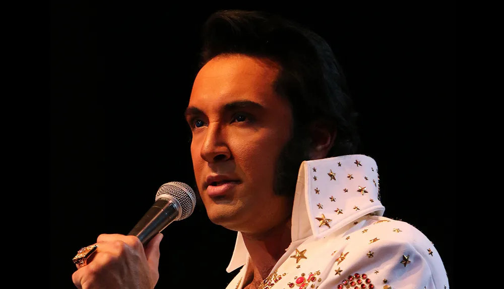 A person wearing an Elvis Presley-style costume is holding a microphone presumably performing or about to perform