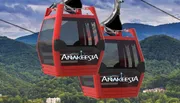 The image shows red gondola cabins of a cable car system against a backdrop of lush green mountains, presumably serving as a mode of transportation for sightseeing or accessing mountainous areas.