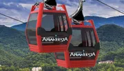 The image shows red gondola cabins of a cable car system against a backdrop of lush green mountains, presumably serving as a mode of transportation for sightseeing or accessing mountainous areas.