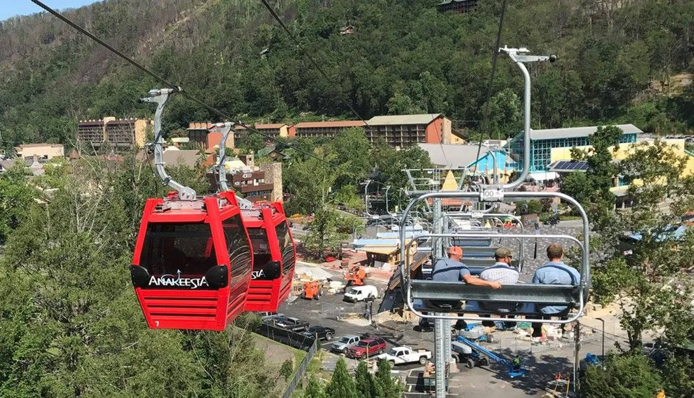 The image displays an aerial view of a chairlift and a gondola system with passengers against a backdrop of greenery and buildings indicative of a mountain resort area