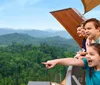 A family is enjoying a scenic view from inside a cable car ride surrounded by lush green forests under a blue sky