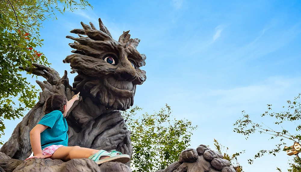 A child in a blue shirt is pointing at a large whimsical tree-like statue with a face against a clear blue sky