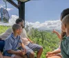 A family is enjoying a scenic view from inside a cable car ride surrounded by lush green forests under a blue sky
