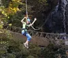 A smiling child wearing a helmet and harness joyfully zip-lines against a backdrop of trees and a waterfall