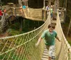 A smiling child wearing a helmet and harness joyfully zip-lines against a backdrop of trees and a waterfall