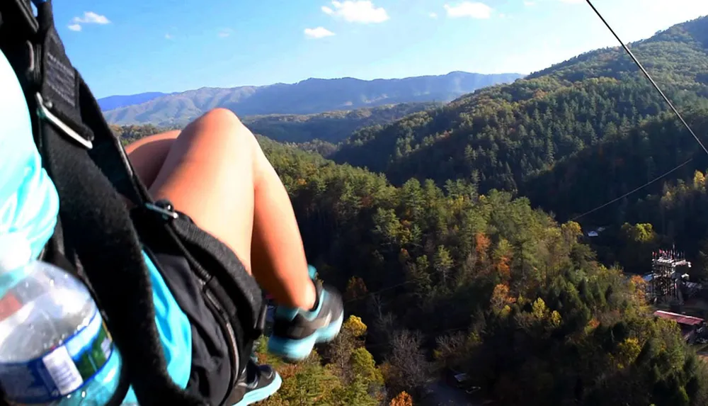 A person is ziplining above a forested valley with mountains in the distance