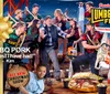 The image depicts a lively and colorful promotional scene for Paula Deens Lumberjack Feud Christmas Supper Show featuring a playful group of people dressed as lumberjacks along with a child in the foreground and a character dressed as Santa Claus holding a chainsaw