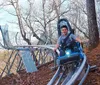 An adult and a child are raising their arms in excitement while riding a blue alpine coaster amidst a lush green landscape