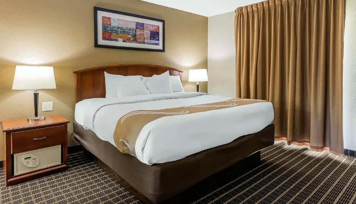 The image shows a neatly arranged hotel room with a large bed side table lamps and a decorative picture above the bed