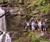 A group of six people are smiling for a photo beside a rocky waterfall