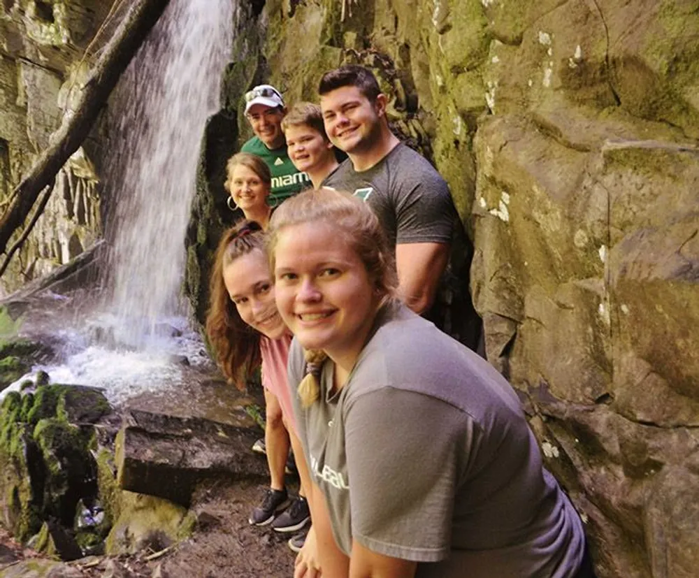 A group of six people are smiling for a photo beside a rocky waterfall