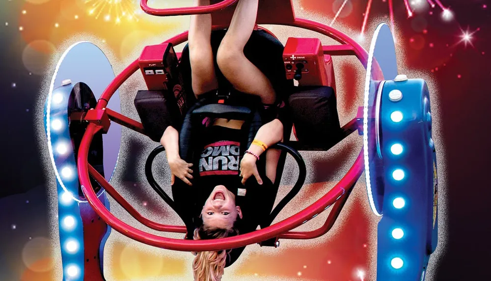 A person is upside down secured in a roller coaster seat with a joyful expression amidst a colorful backdrop that suggests movement and excitement