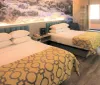 The image shows a modernly furnished hotel room with two twin beds with patterned yellow covers a nature-themed mural behind the beds wooden flooring and a window with curtains