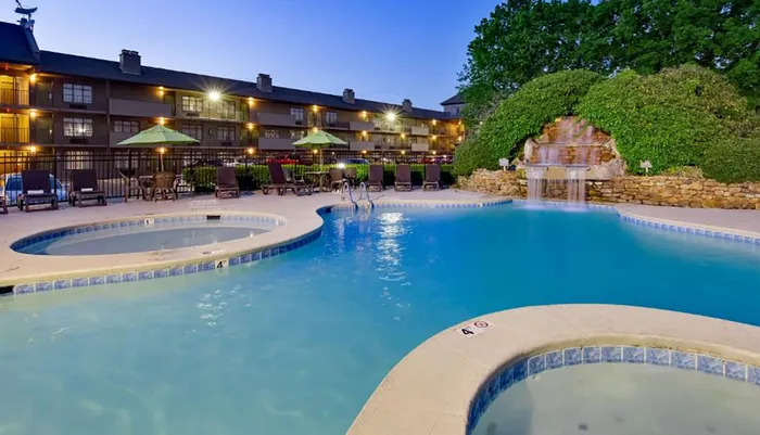 An inviting hotel pool area with loungers a hot tub and a waterfall feature taken at dusk