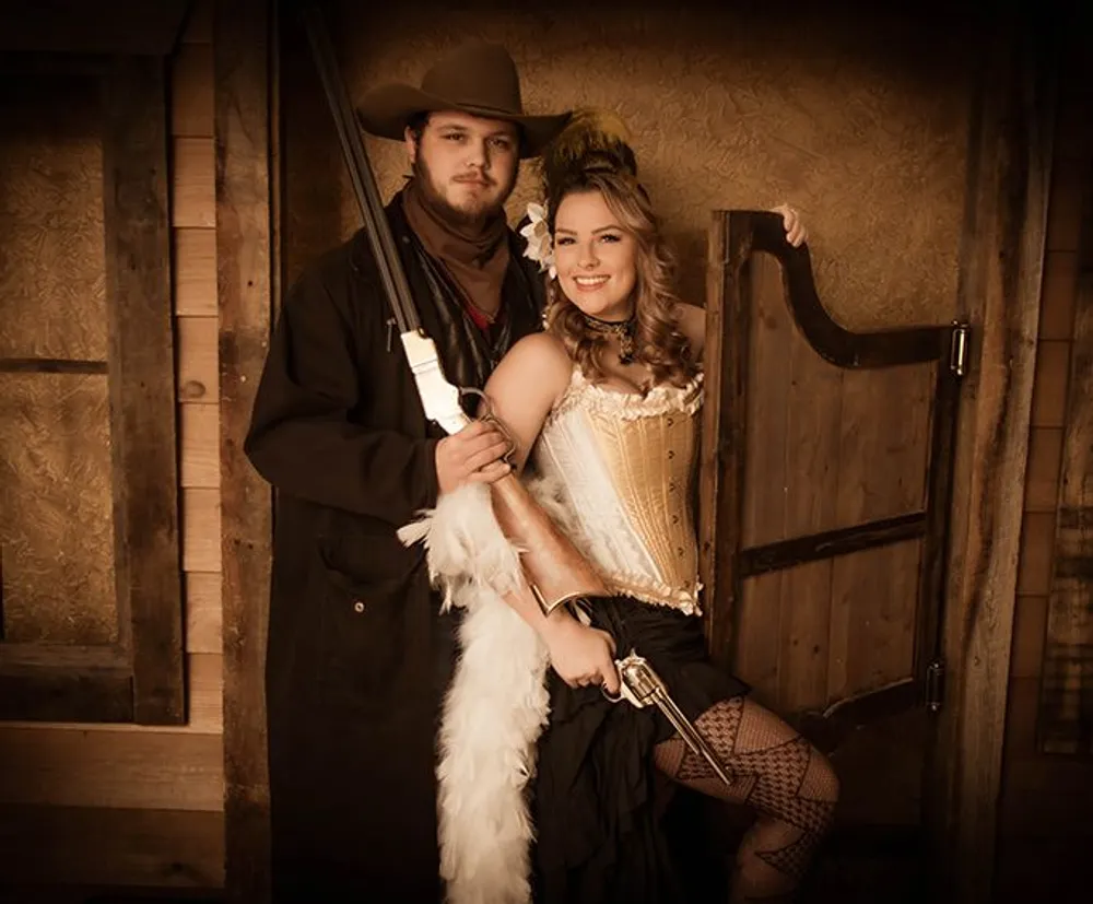 A man and a woman are dressed in Western-themed costumes posing with props that evoke the Wild West era