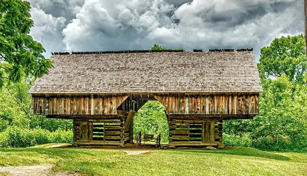 A rustic wooden covered bridge stands in a lush green environment under a cloudy sky