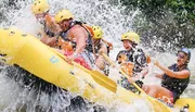 A group of people wearing life jackets and helmets are joyfully white water rafting, splashing through a rapid.