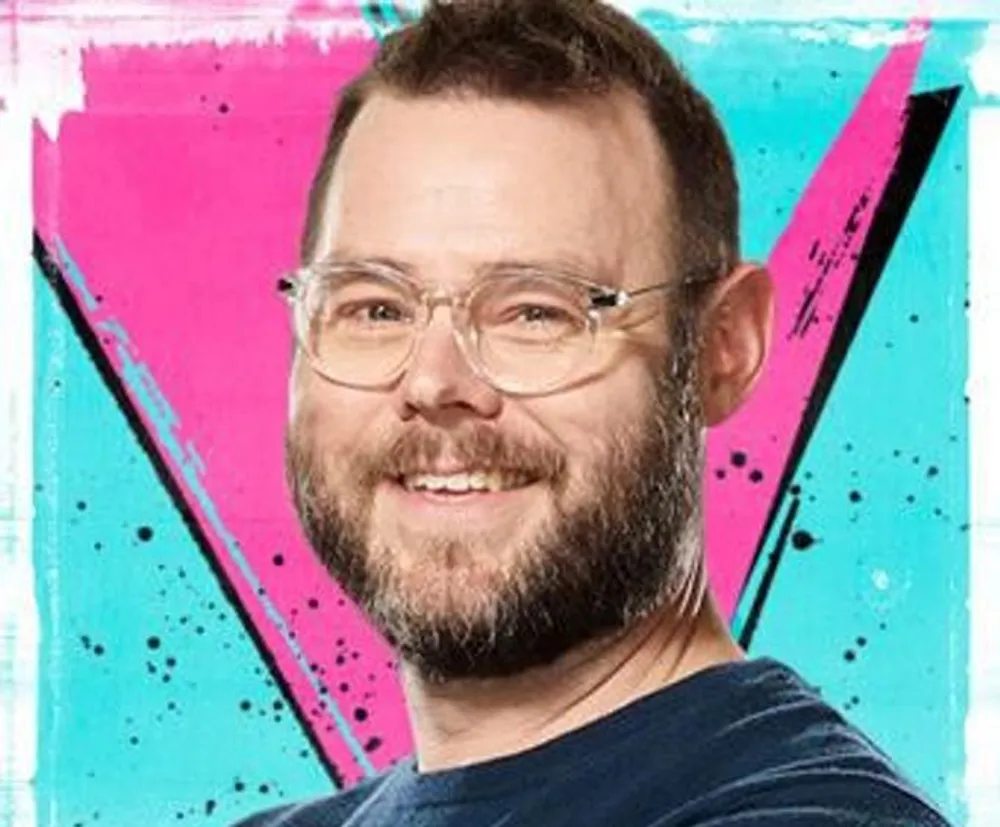 The image shows a smiling man with glasses in front of a vibrant pink and blue graffiti-styled background