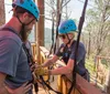 Three people are enjoying a zip-line adventure through a forested area with two of them actively gliding down the line while another waits on a platform