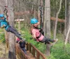 Three people are enjoying a zip-line adventure through a forested area with two of them actively gliding down the line while another waits on a platform