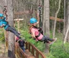 Three people are enjoying a zip-line adventure through a forested area with two of them actively gliding down the line while another waits on a platform