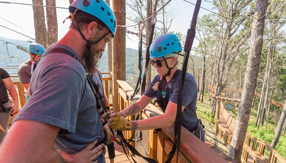 People wearing helmets and harnesses prepare for a zipline adventure in a wooded area