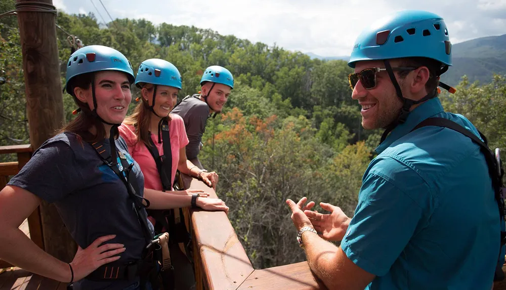 A group of people wearing blue helmets and safety gear are smiling and talking on a wooden platform overlooking a forest