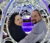 A smiling couple is sitting inside an ornate light-adorned carriage at night