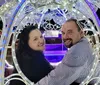 A smiling couple is sitting inside an ornate light-adorned carriage at night