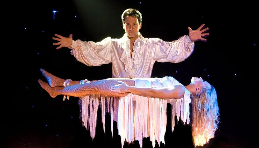A magician performs a levitation illusion with a woman seemingly floating in mid-air on stage