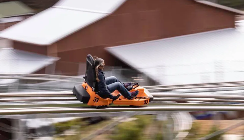 A person is enjoying a ride on an orange alpine coaster captured with a motion blur effect to emphasize speed
